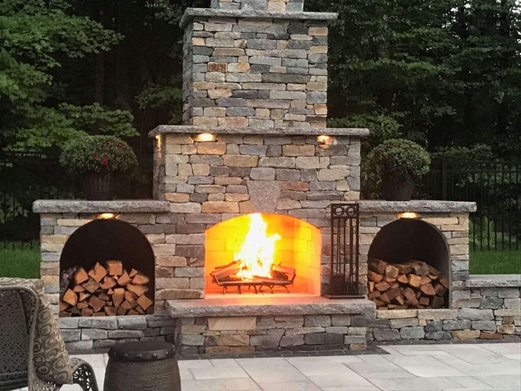 Outdoor Ottawa Ontario Stone fireplace and wood alcove with bright burning fire at dusk.